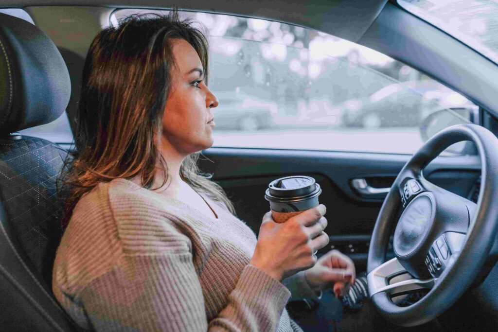 Kvinde i bil med kaffe i hånden